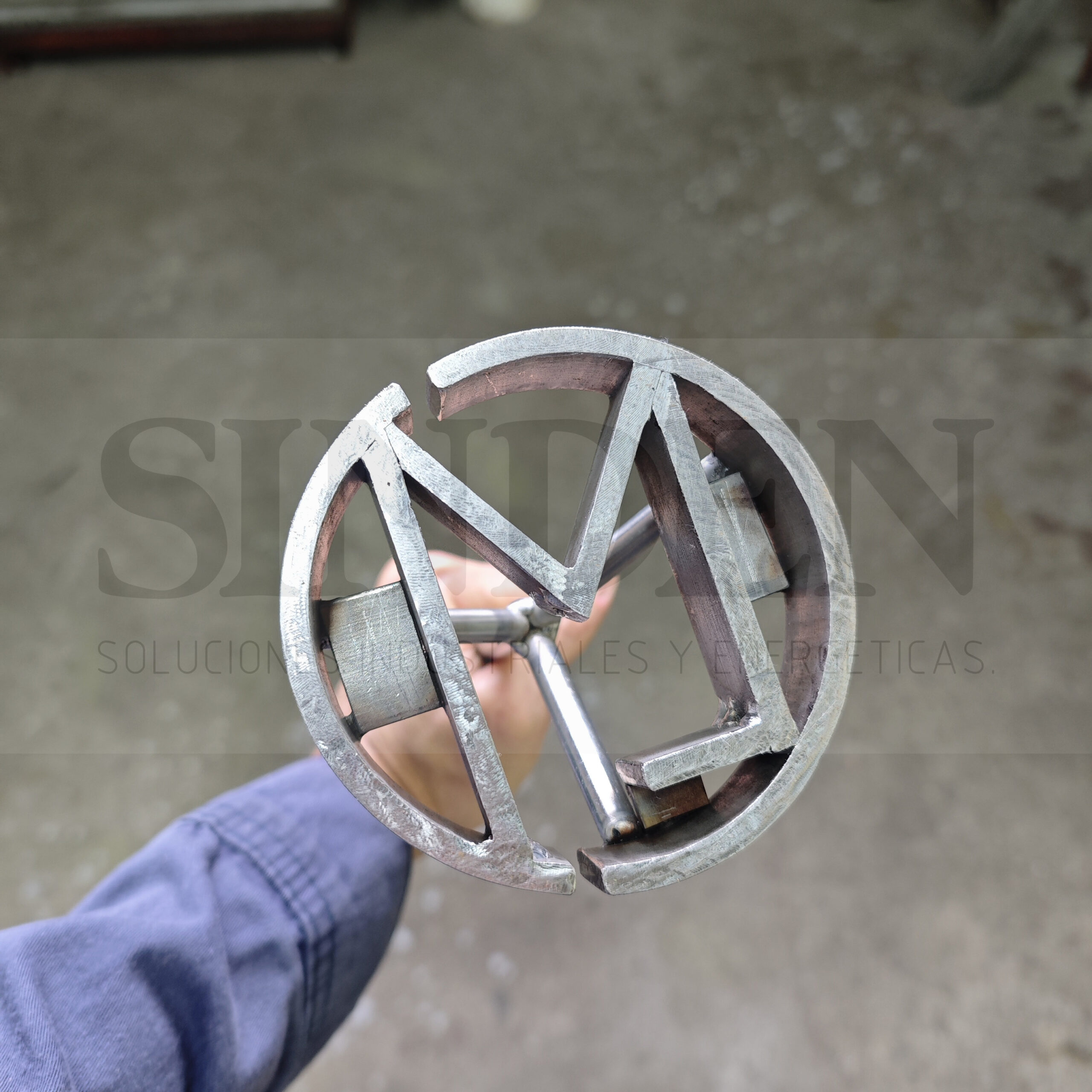 Marca circular con letra M en acero inoxidable, sostenida en la mano